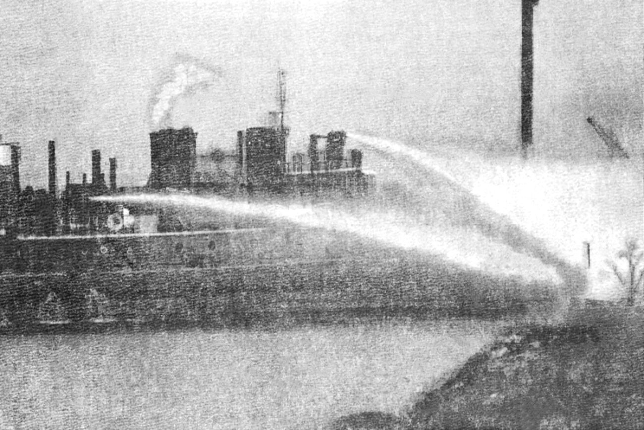 grey and white photo of water coming out of boat trying to contain a fire