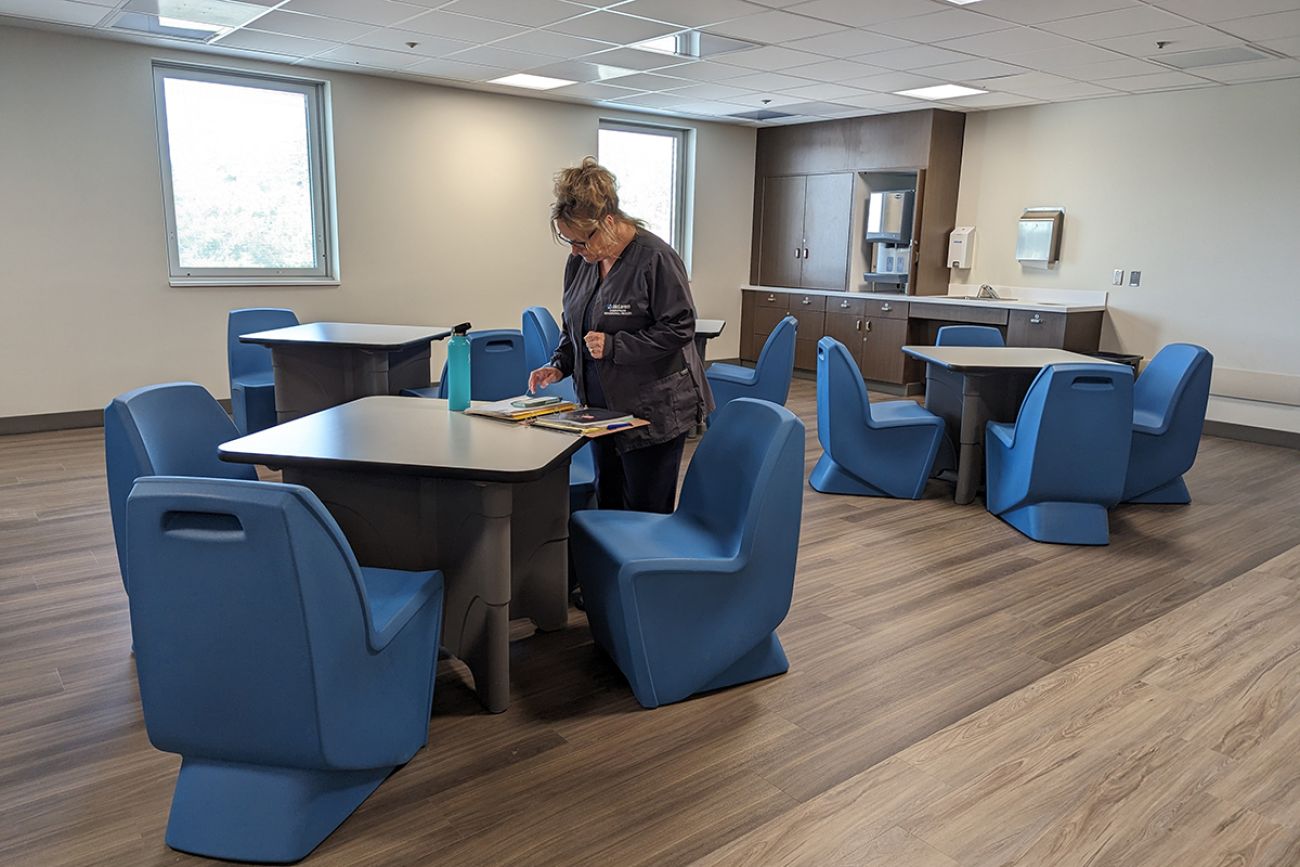 room with tables and blue chairs. empty except for one woman