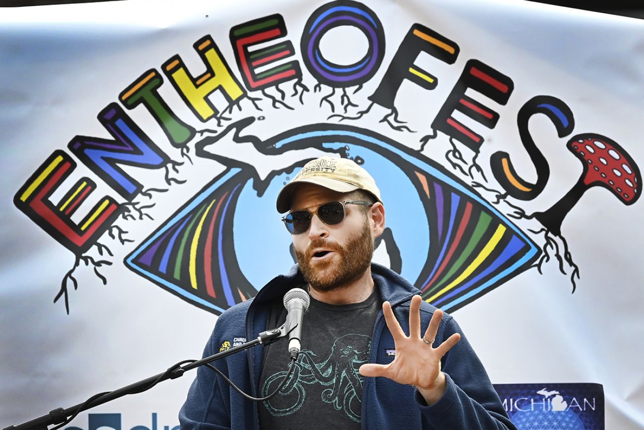 Kevin Boehnke speaking into a microphone. A banner that says "Entheofest" is behind him