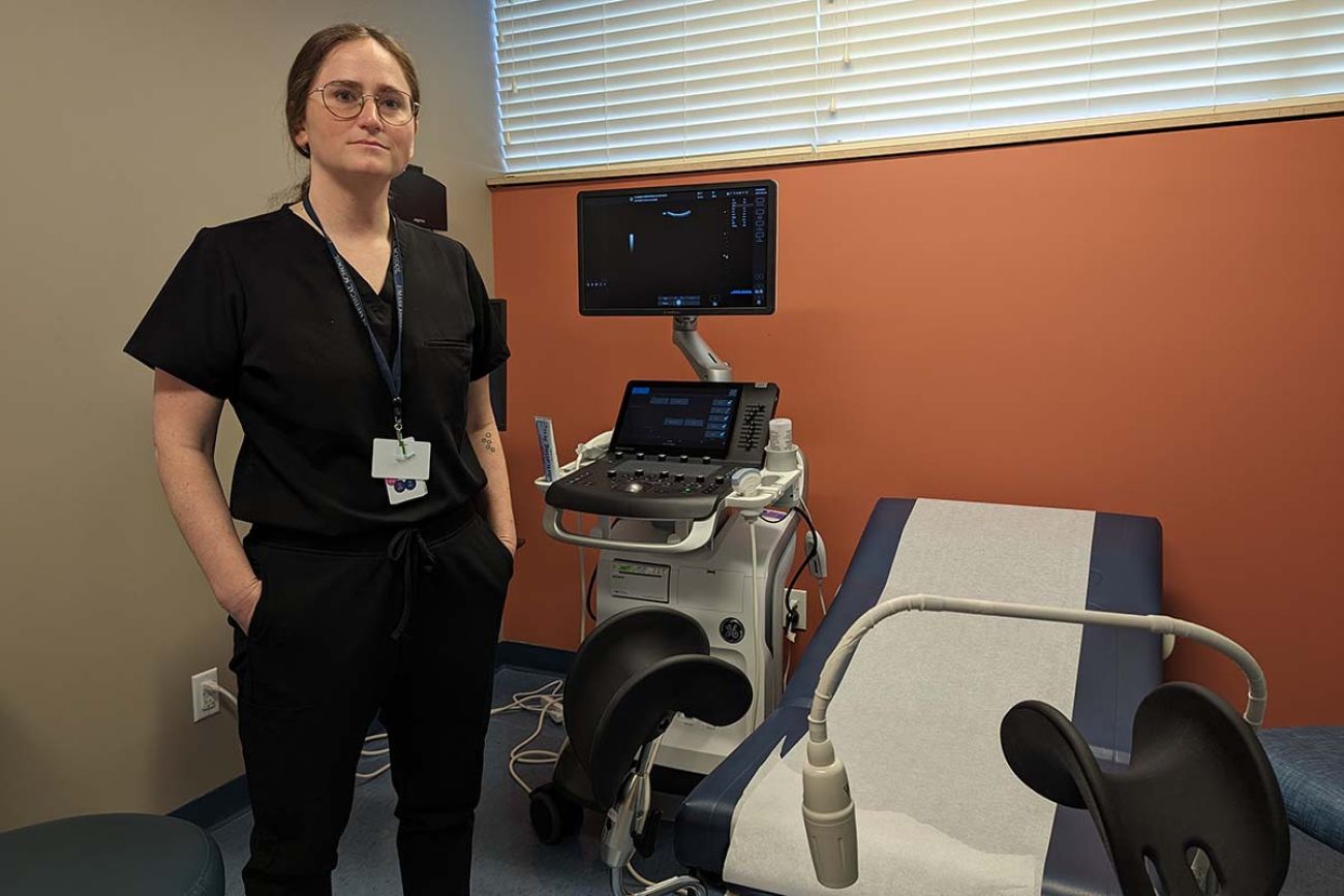 A woman, wearing dark-colored scrubs, is standing in doctor's office