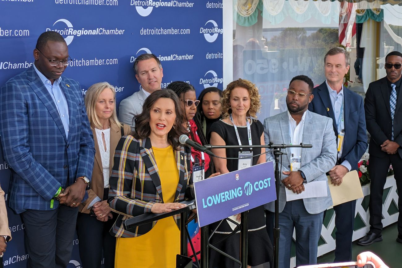 Gov. Gretchen Whitmer speaking into a microphone, many people standing behind her