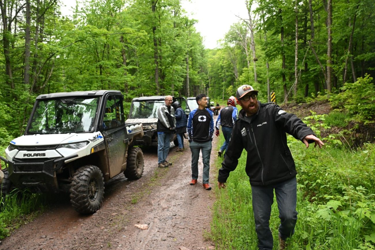 Parked electric vehicles on a dirt road. People are standing by the road