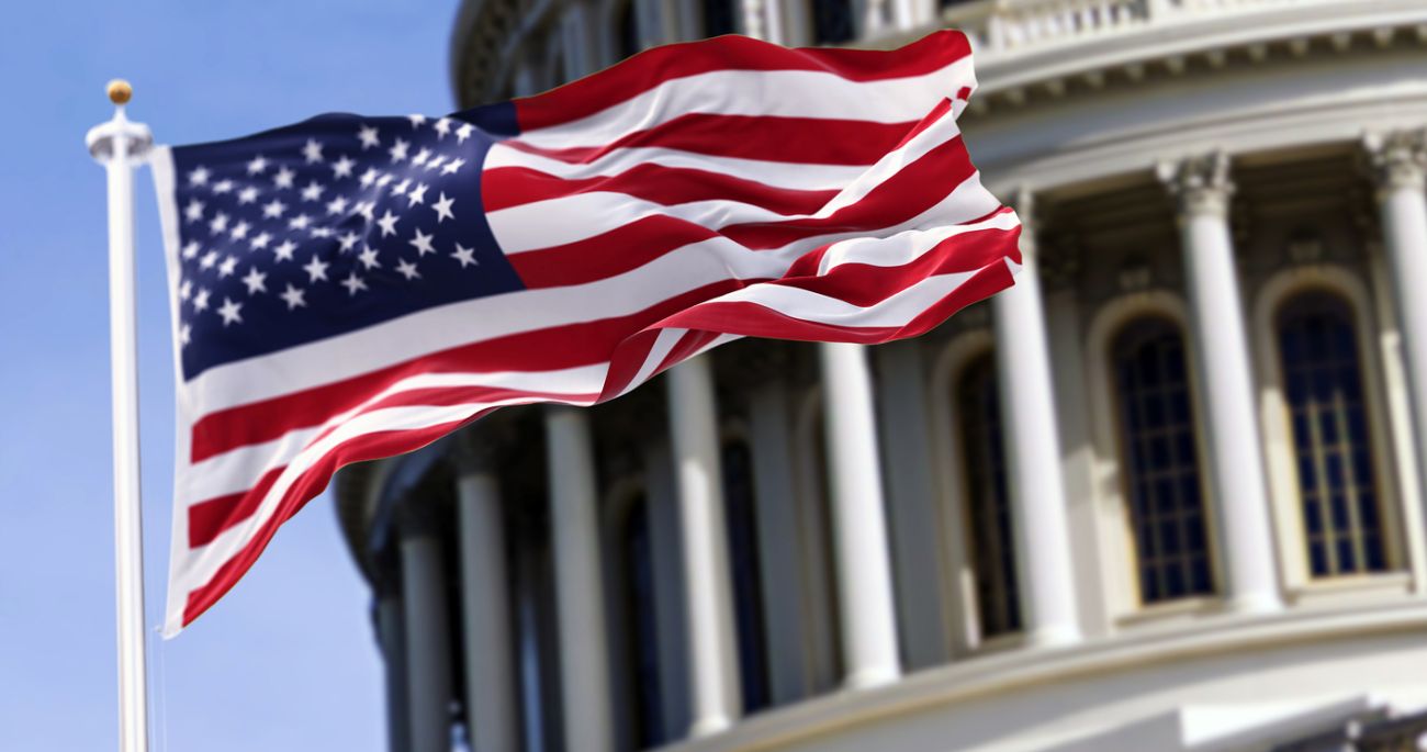  The flag of the united states of america flying in front of the capitol building blurred in the background. 