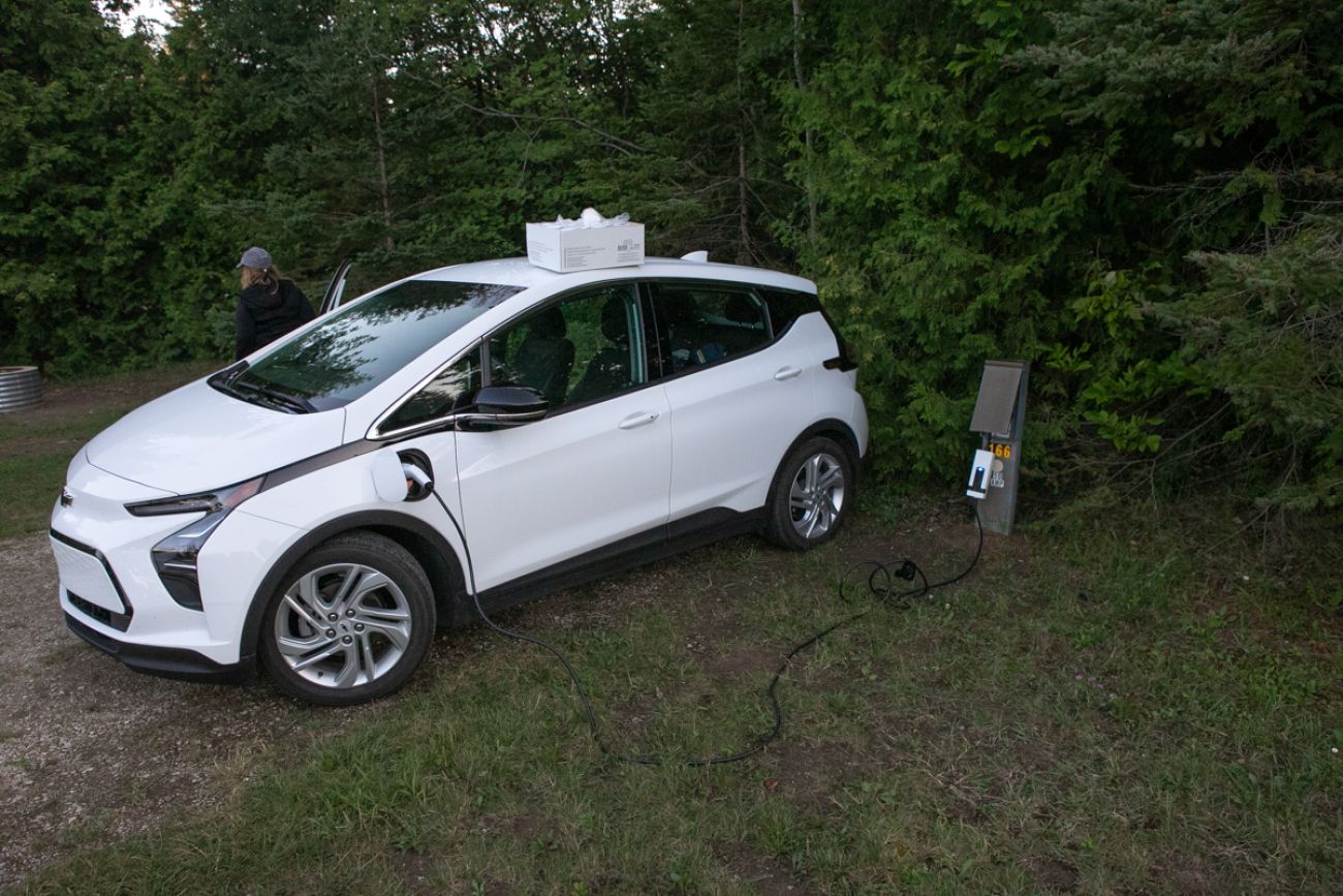 A white Chevy bolt being charged at a gas station