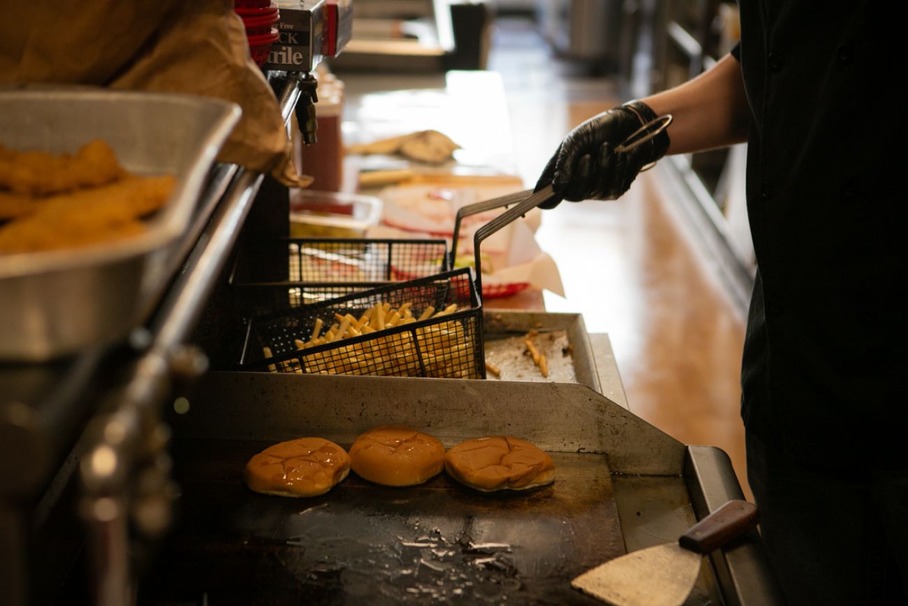 Someone cooking burgers and putting fries in the fryer