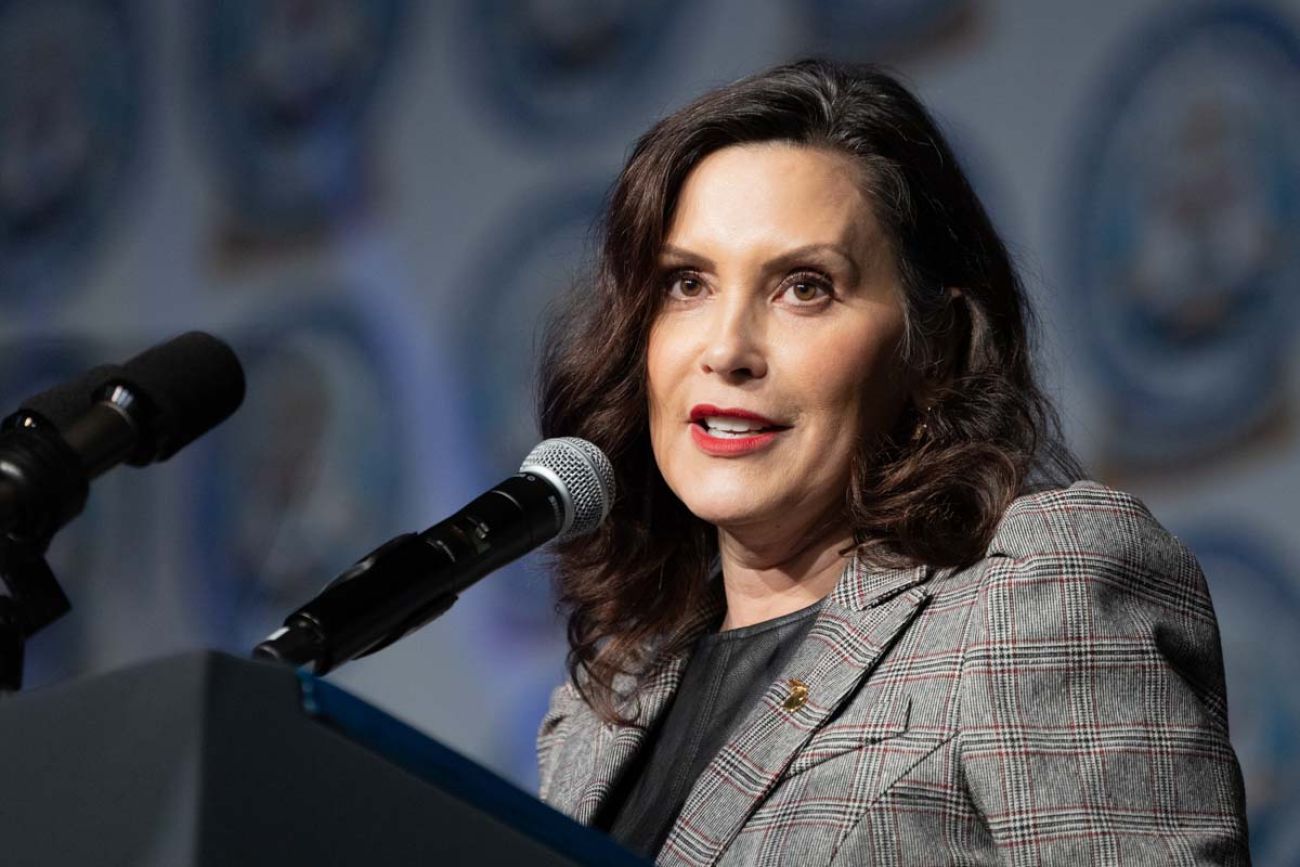Gov. Gretchen Whitmer, wearing a grey jacket, speaks into a microphone