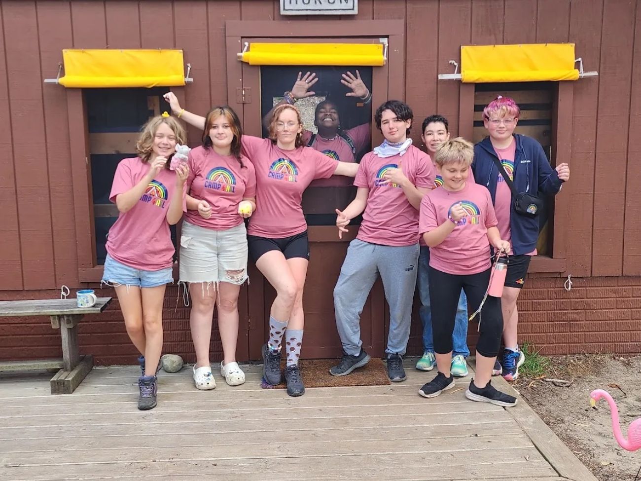 A group of teens with pink shirts in front of the cabin