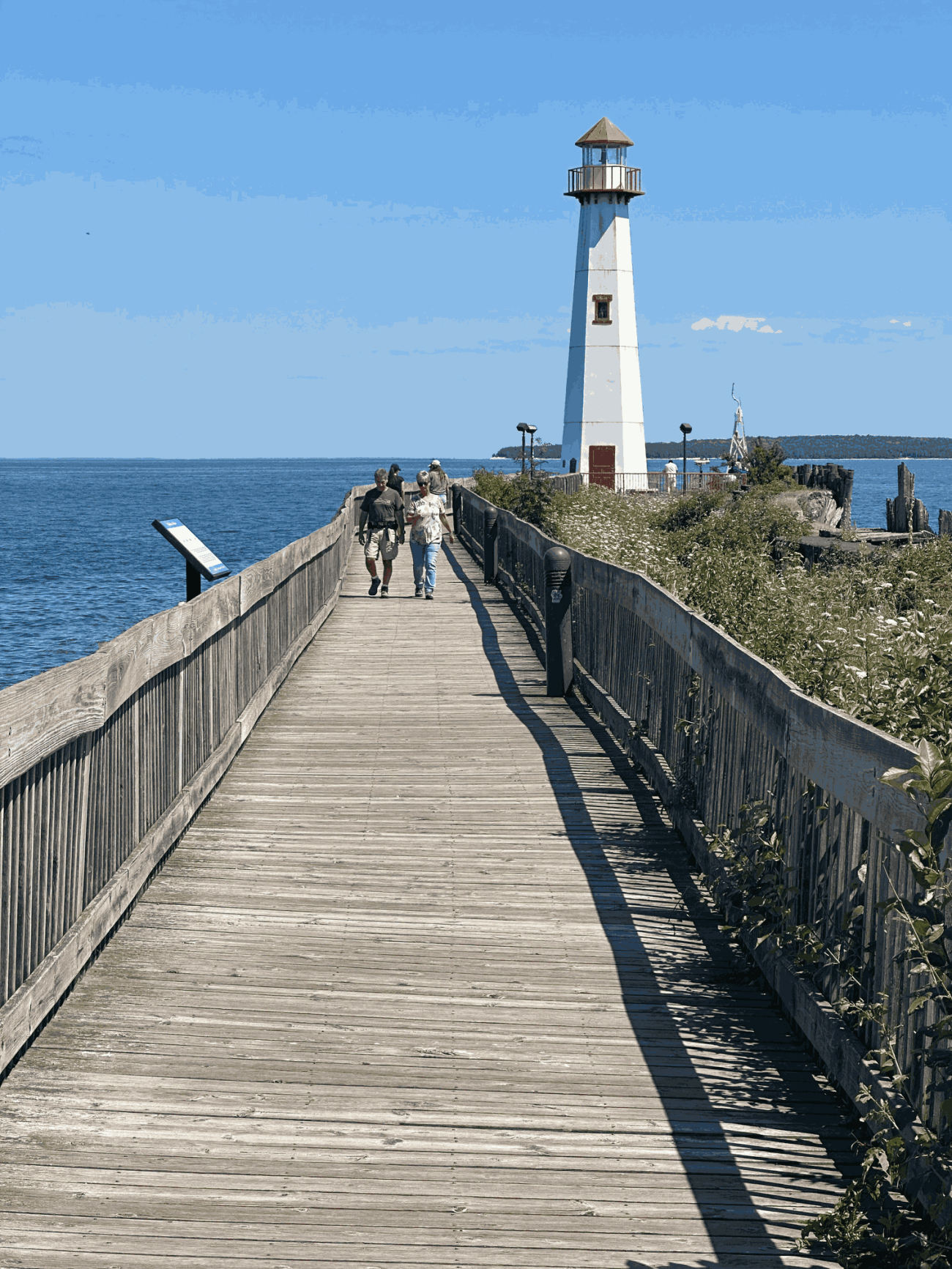 A lighthouse at St. Ignace, Michigan. People are walking on the boardwalk leading to the lighthouse