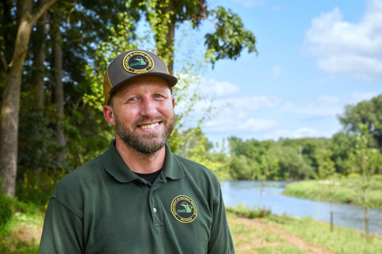 Mark Mills outside, posing for a photo. He is wearing a green Michigan DNR shirt