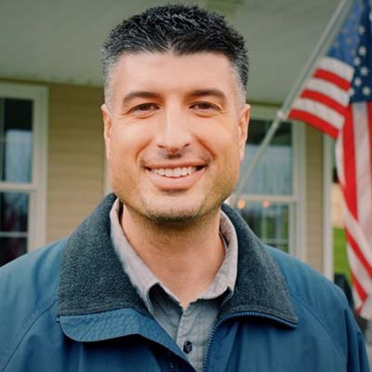 Tom Barrett posing for a picture in front of home with an American flag