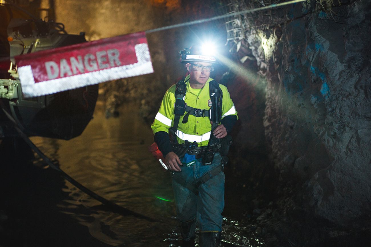 Andy Vaughn, wearing a hard hat with a light on it, walks through a dark mine. You can see a danger sign