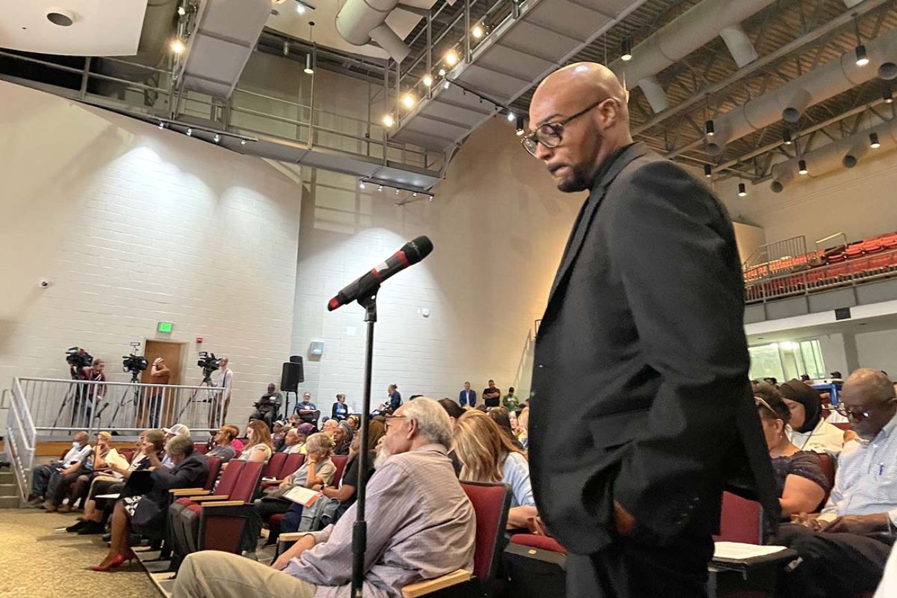 Detroiter Khary Frazier, wearing a black suit, speaks into a microphone. People are sitting behind him