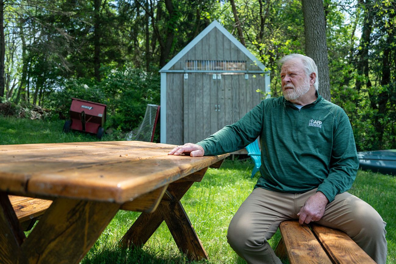  Dr. Glenn Dregansky, wearing a green sweater, sits outside on a picnic table 