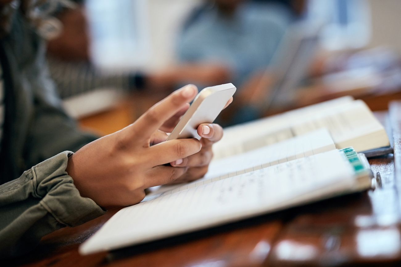 Child holding cell phone. On desk is a notebook