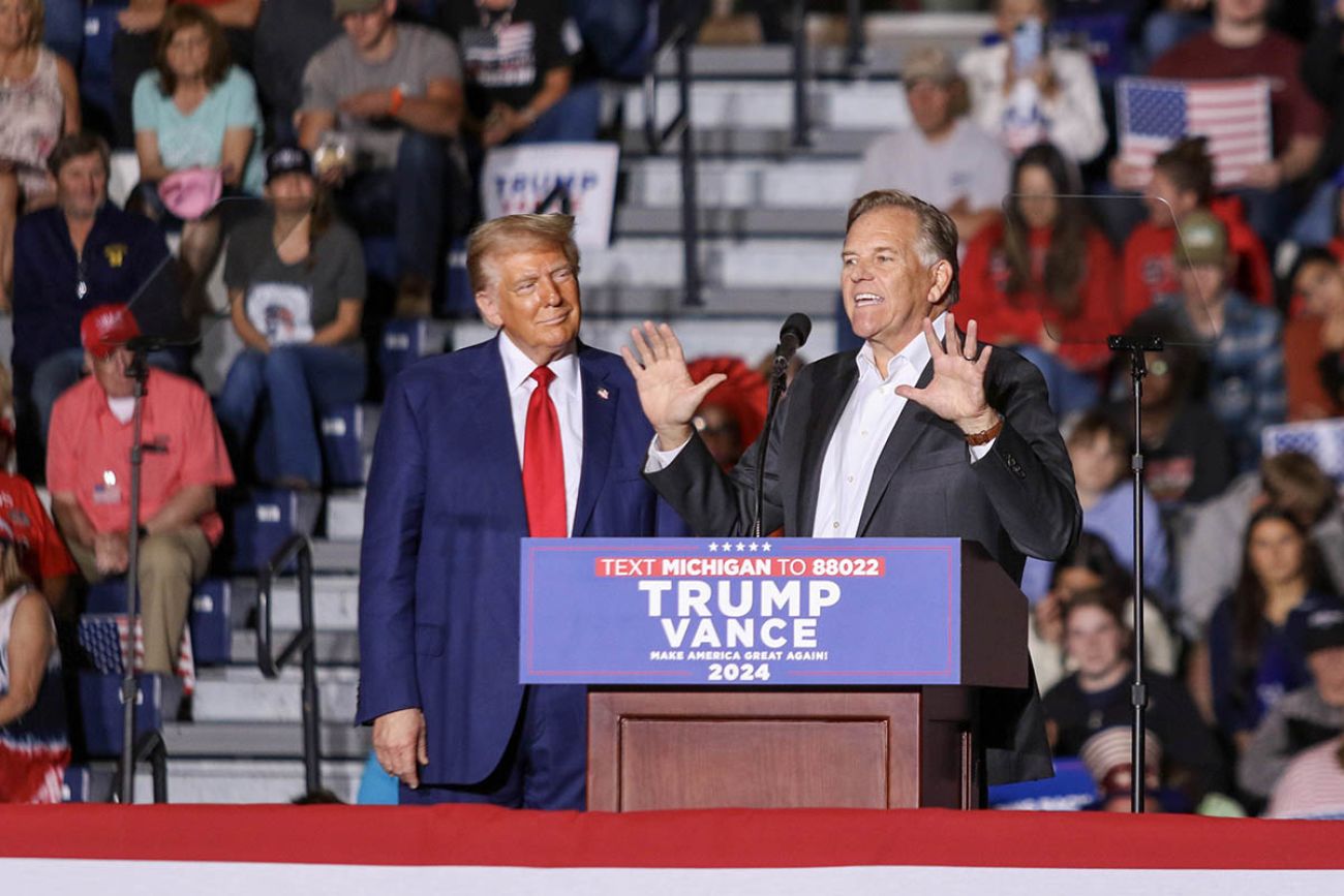 Mike Rogers stands at a stage next to Donald Trump at an event in Michigan