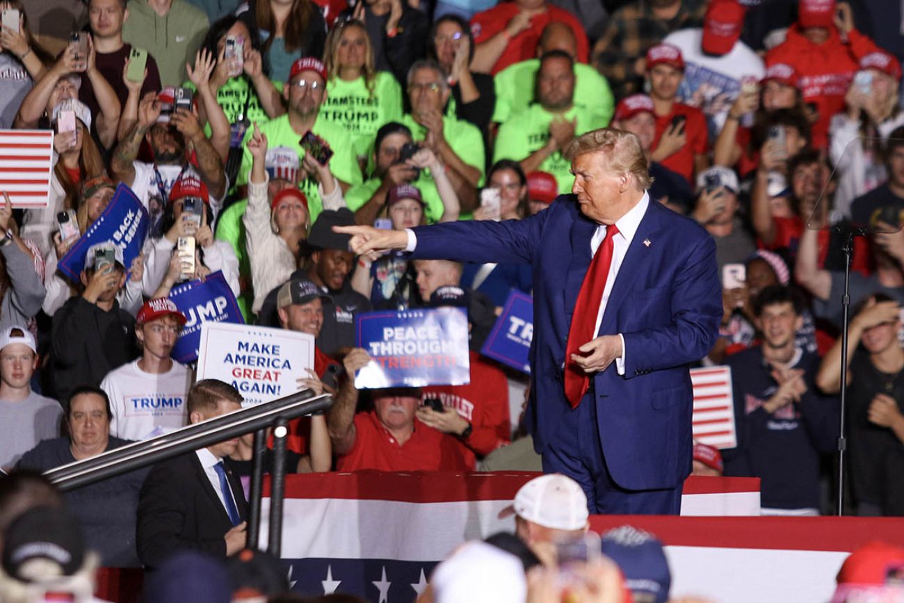 Former President Donald Trump, wearing a blue suit, points to the crowd