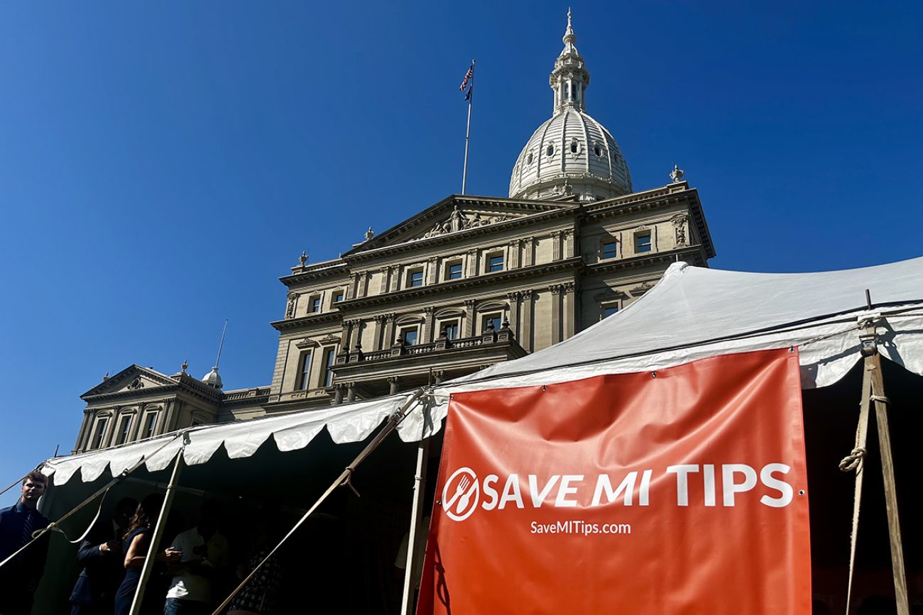 A red sign in front of the Michigan capitol building that says "Save MI Tips"