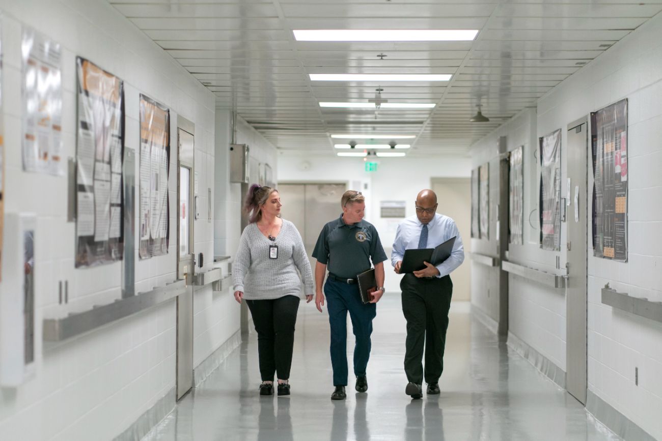 One woman and two men walk down a hospital hall.