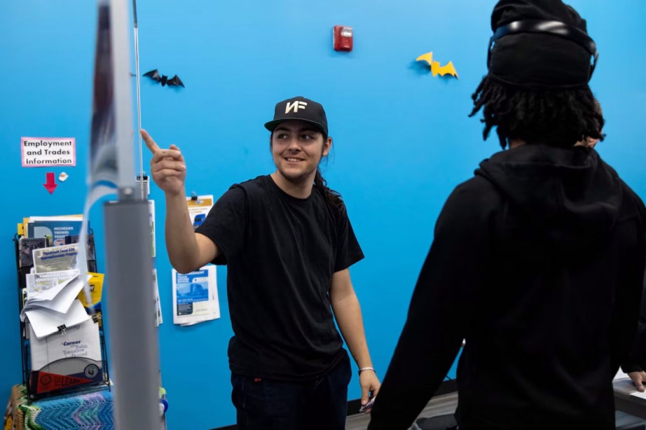 Lucian talks to another student in a classroom with blue walls