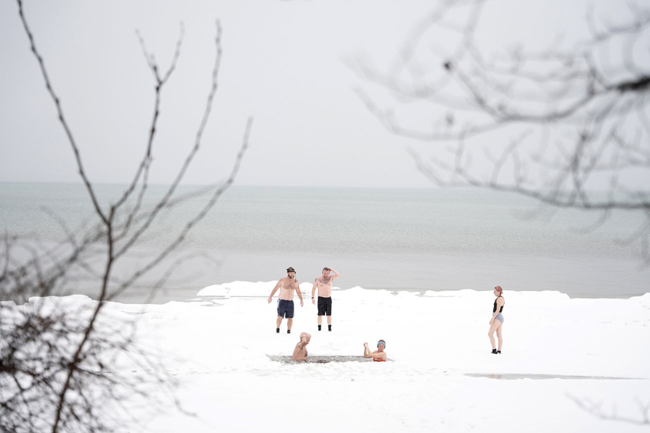 People standing in the snow. A couple of people are in the water. 