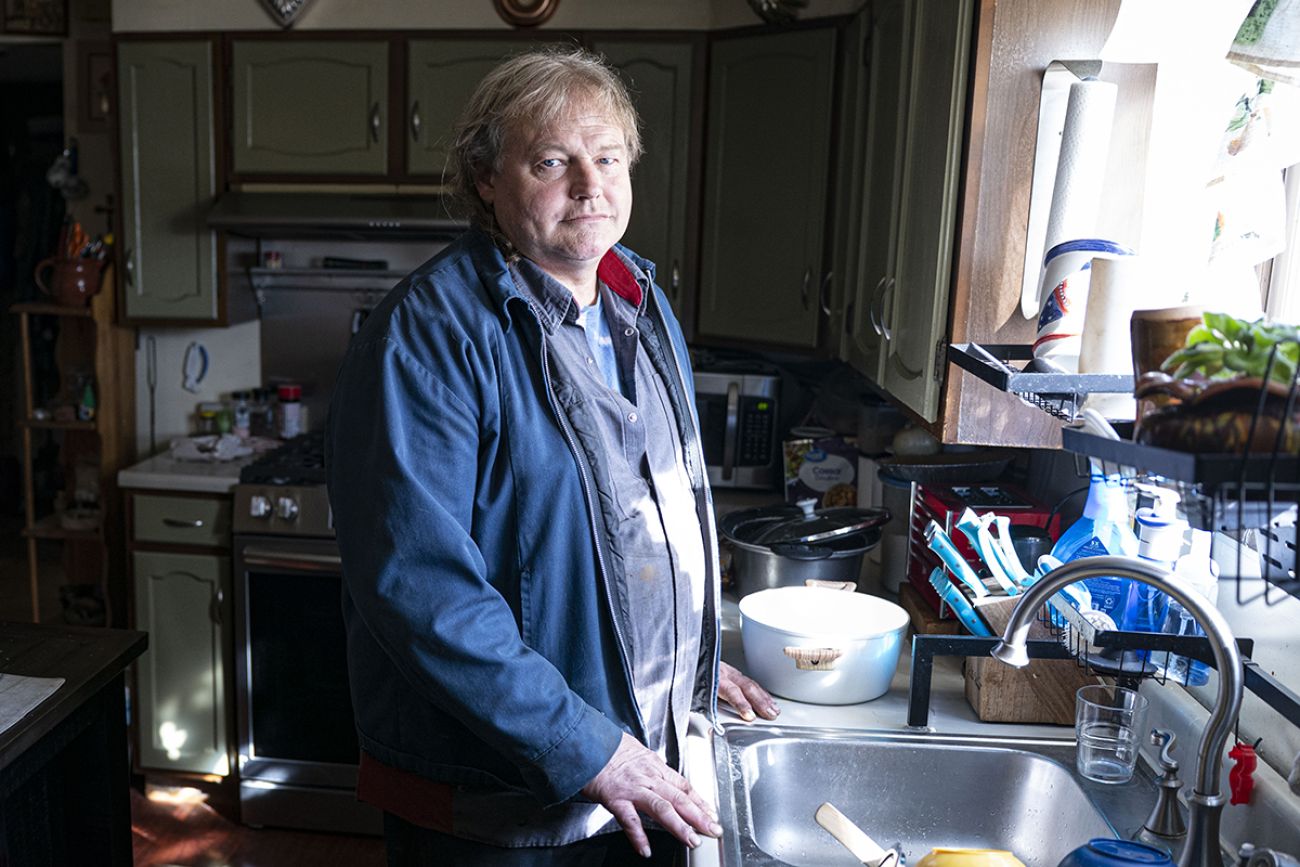 JT Anderson near the kitchen sink in his home. He is wearing a blue jacket.