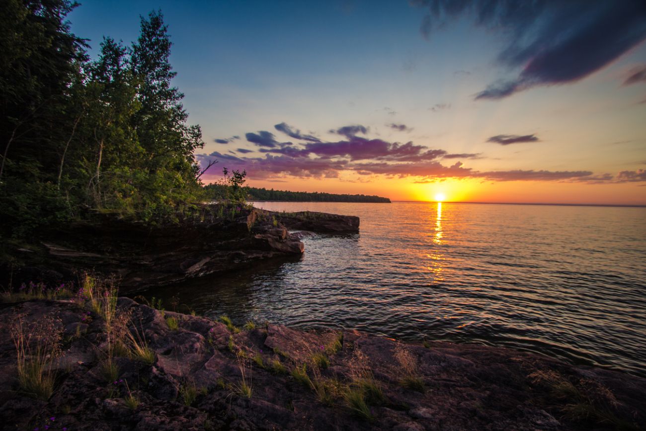 A sunset on a lake. You can also see trees. 