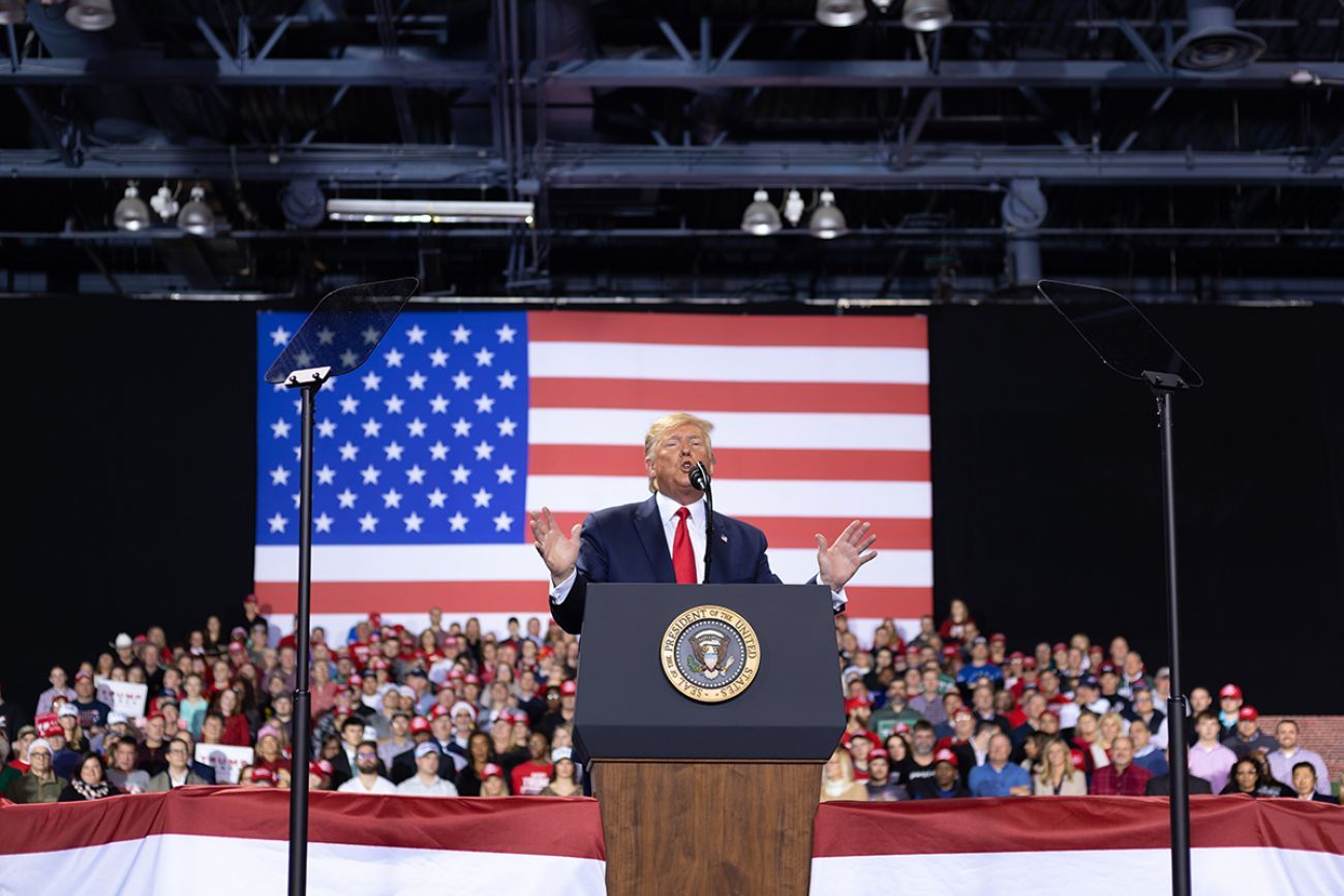 Donald Trump on a stage. People are behind him. 