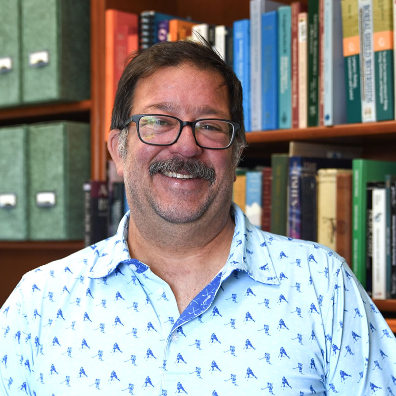 Andrew Muir poses for a photo in front of a bookshelf.