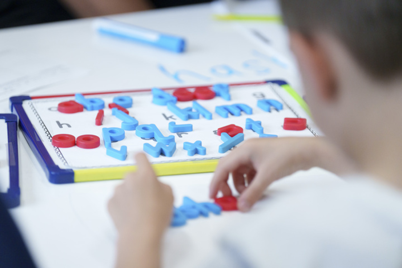 A view of a child from the back. The student is participating in an activity that focuses on practicing letters.