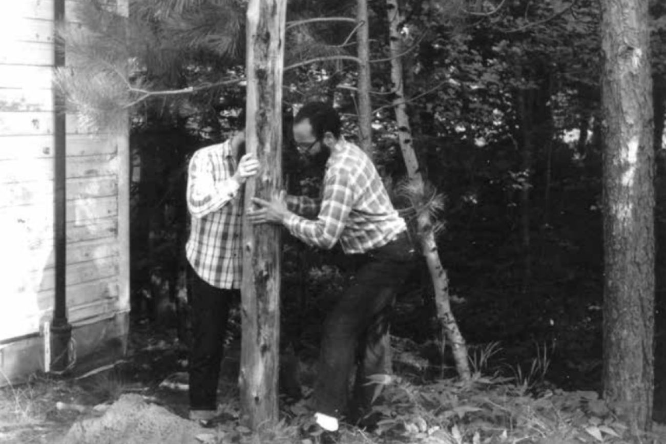 A black and white photo shows two men driving a post into the ground