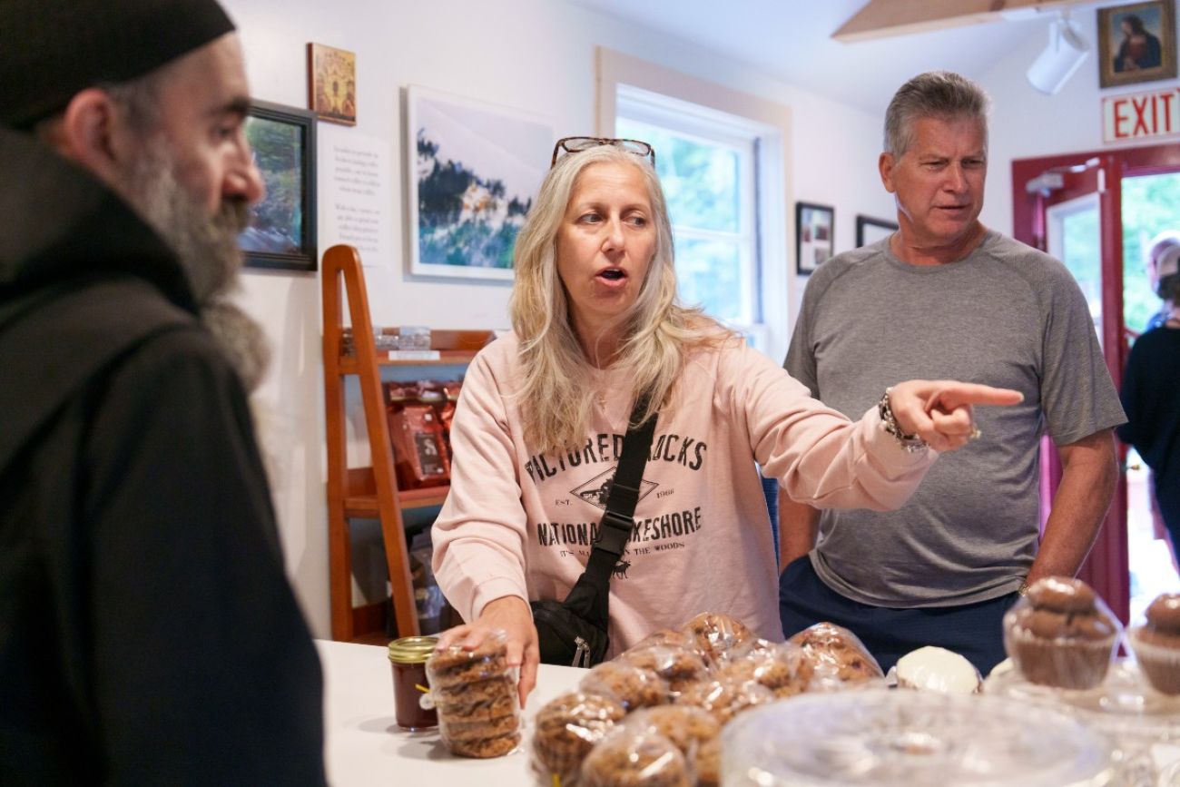 A man stands behind the counter at a bakery talking to customers on the other side of the counter