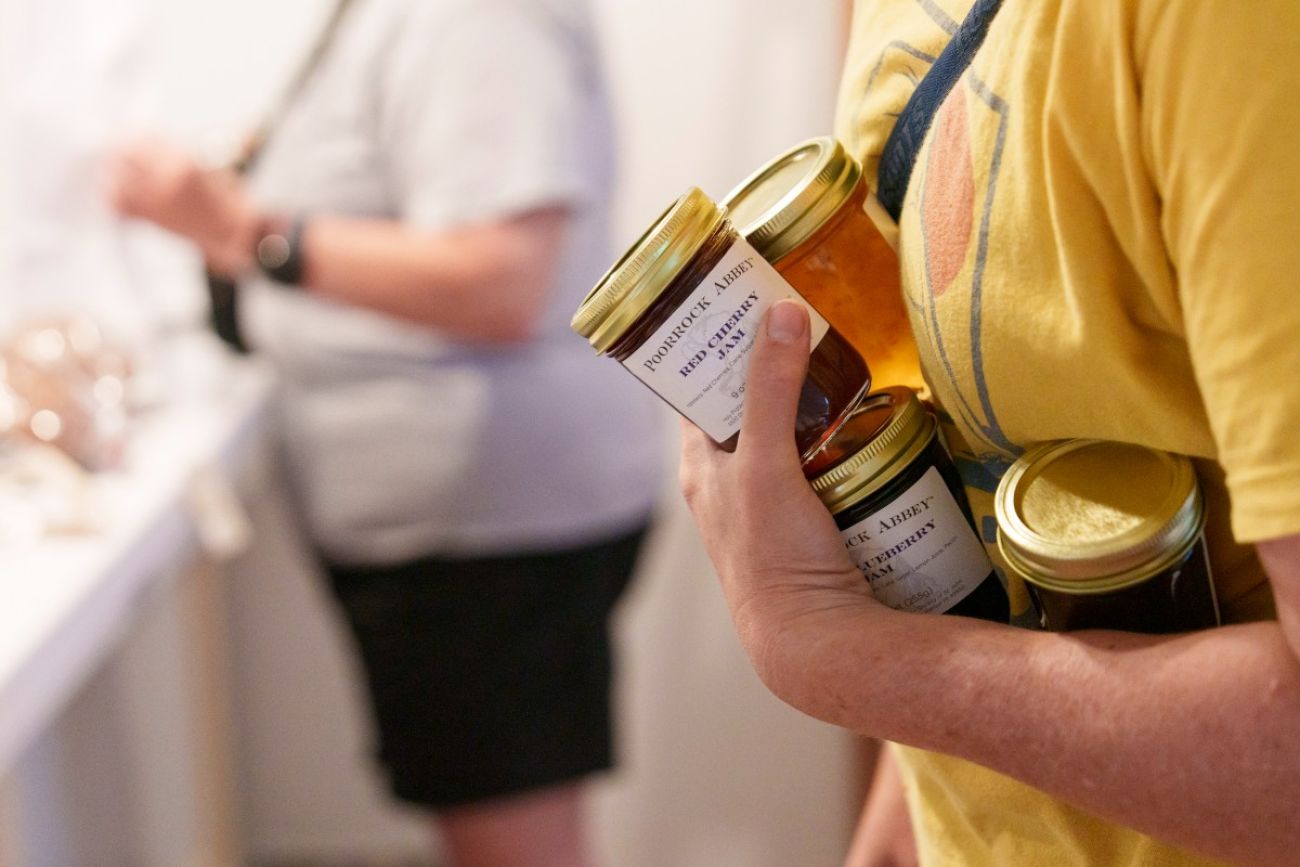 Customers stand in line at a baker and one of the customers holds several jars of jam