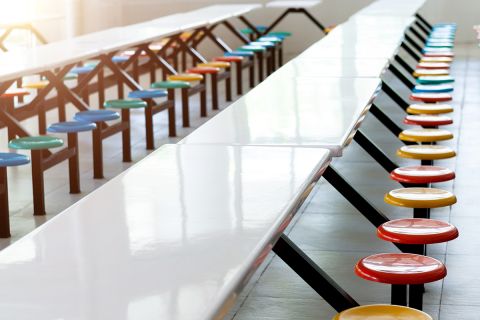 Clean school cafeteria with white tables and colorful seats