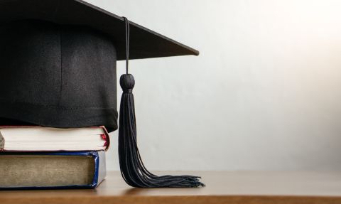  Mortar board with degree paper and books on wood table