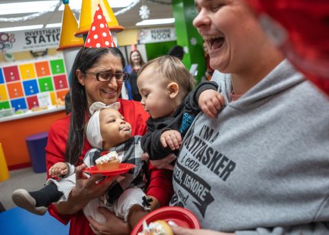 Flint pediatrician Dr. Mona Hanna with babies. She is wearing a birthday hat. 