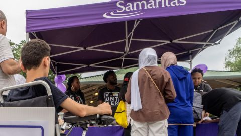 People approach a purple Samaritas tent. 