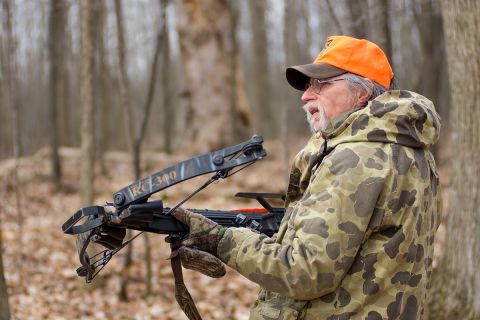 A man holding a bow in the woods. 