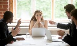 multiple men talking and pointing at a woman in a board room