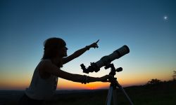 Young woman looking at the sky with a astronomical telescope.