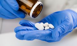 medical practitioner wearing blue surgical latex gloves holding medicine bottle,taking out several white pills