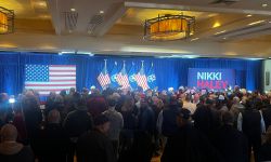 A crowd of people standing in a ballroom at the Detroit Marriott in Troy waiting for GOP presidential candidate Nikki Haley. Facing them are an American flag and Nikki Haley sign.