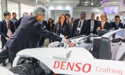 Gov. Gretchen Whitmer surrounded by many other people looking at a white Denso vehicle