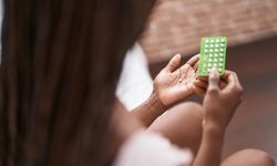 African american woman holding birth control pills sitting on bed at bedroom