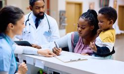 African American mother holding her small son while filling medical paperwork at reception desk in the hospital.