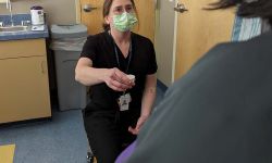 A woman in dark-colored scrubs and a face masks holding a cup of pills 