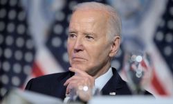 President Joe Biden with his hand on his chin. There are American flags in the background