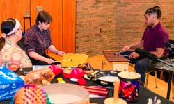 Three people sitting in a room, playing instruments 