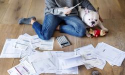 Woman sits on the floor with her white dog. Bills are on the floor