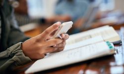 Child holding cell phone. On desk is a notebook