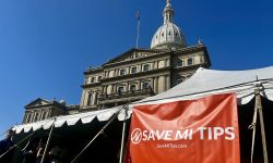 A red sign that says "Save MI Tips" in front of the Michigan Capitol Building 